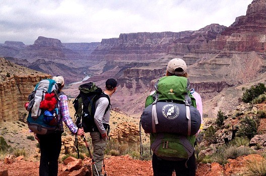 three hikers with backpacks looking out at the grand canyon