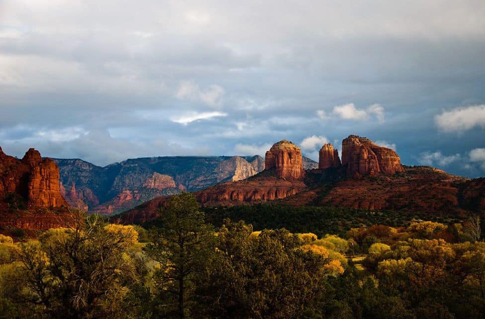 a view of tall red rock formations behind green and yellow trees