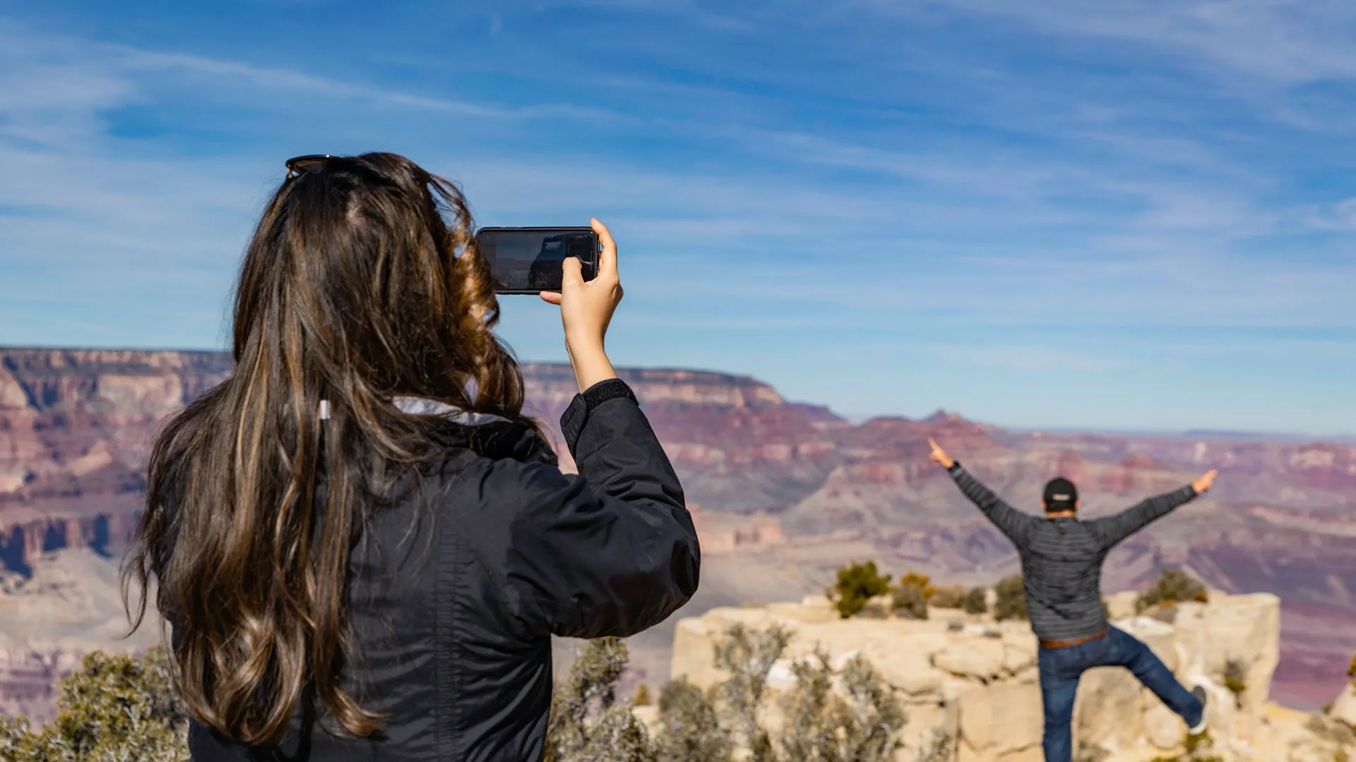 woman taking a picture of another person with the grand canyon in the backgound