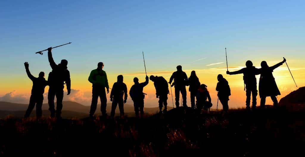 silhouette of group standing in front of a sunset