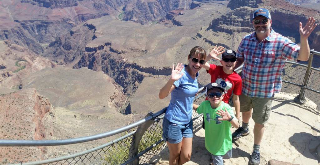 family of parents and two boys smiling and waving for a photo at the grand canyon