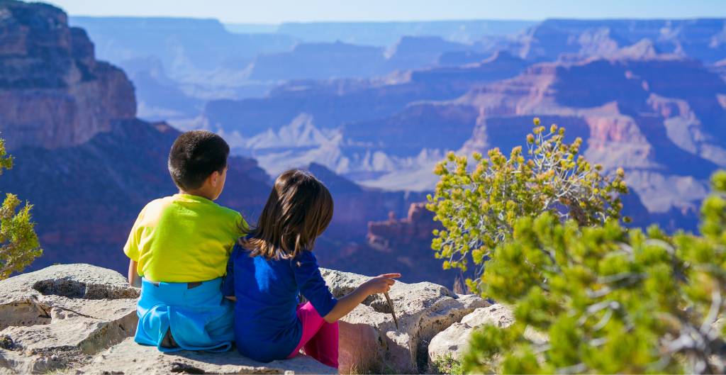 two kids sitting at the edge of the grand canyon with dramatic rock layers in view