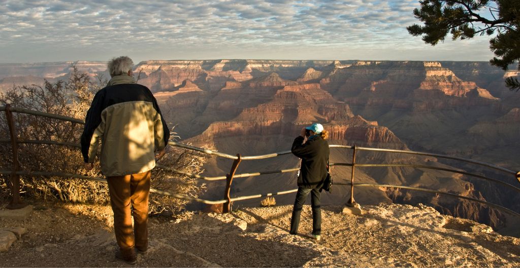 woman taking photo of grand canyon in golden light with man standing nearby