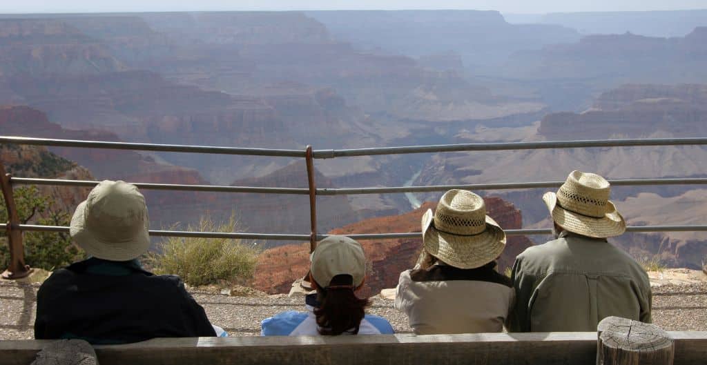 group of four wearing hats sitting on a bench looking out at the grand canyon