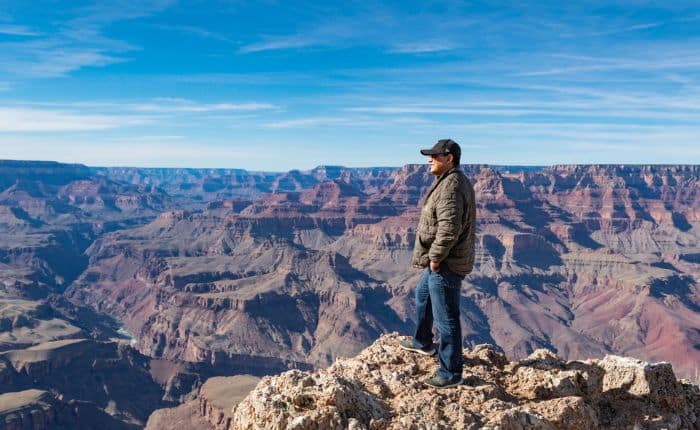 man standing on a ledge looking out at the grand canyon