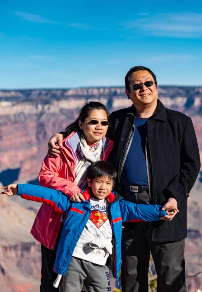 A family of three pose in front of a Grand Canyon overlook