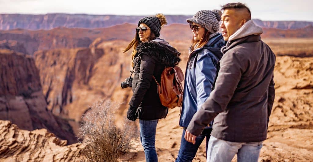 A group of three walks around the grand canyon in jackets